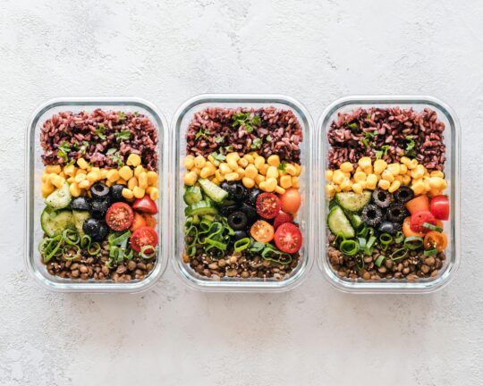 Meal Prep – das klingt modern und praktisch, aber letztlich handelt es sich um die zeitlose Kunst des Vorkochens, neu gedacht und mit dem Fokus auf individuellen Bedürfnissen und zeitgemäßer Technik. Für Athleten und ihre Coaches, die durch knappe Zeitpläne und hohe Leistungsansprüche gefordert sind, bietet Meal Prep eine Lösung, die weit über Bequemlichkeit hinausgeht. Es geht darum, sich gesund und leistungsfördernd zu ernähren – auch in stressigen Phasen zwischen Training und Wettkampf. In einem aufschlussreichen Gespräch mit der Rezeptentwicklerin Lena Merz, die auch das Buch „Meal Prep“ verfasst hat, wird klar, dass diese Methode nicht nur für Kochliebhaber, sondern für jedermann geeignet ist, der seinen Alltag effizienter und nachhaltiger gestalten will. Aber wie funktioniert das eigentlich? Und warum könnte Meal Prep für Athleten eine Revolution im Speiseplan bedeuten? Die Vorteile von Meal Prep für Sportler und Coaches Die Basis von Meal Prep ist einfach: Mahlzeiten im Voraus planen und zubereiten, um im Alltag stets auf hochwertige, ausgewogene Gerichte zurückgreifen zu können. Für Sportlerinnen und Sportler, die oft zwischen Trainingseinheiten pendeln, ist das ein unschätzbarer Vorteil. Statt auf Fast Food oder unzureichende Snacks angewiesen zu sein, wartet eine gesunde Mahlzeit in der Tasche – perfekt portioniert, nahrhaft und individuell abgestimmt. Zeit sparen durch Struktur: Wer einmal pro Woche ein paar Stunden in die Vorbereitung investiert, kann später an jedem Tag Zeit gewinnen. Lena Merz erklärt, dass sie mit ihrer effizienten Technik in der Lage ist, innerhalb einer Stunde bis zu fünf Gerichte vorzubereiten. Ihr Geheimnis? Cleveres Kombinieren von Ressourcen wie Backofen, Herd, Mikrowelle und kalten Speisen sowie der Einsatz von vorgewaschenem Tiefkühlgemüse, das sowohl Zeit spart als auch voller Nährstoffe steckt. Kostenkontrolle: Die richtige Planung und der gezielte Einkauf reduzieren Verschwendung und sorgen dafür, dass das Budget geschont wird. Kleine Reste können kreativ zu neuen Gerichten verarbeitet werden – aus übrigem Reis entsteht etwa ein Salat, Bratlinge oder ein Auflauf. Individuelle Bedürfnisse: Sportler haben spezifische Anforderungen an ihre Ernährung, abhängig von Trainingsintensität und Zielen. Meal Prep erlaubt es, gezielt auf diese Bedürfnisse einzugehen, sei es durch proteinreiche Speisen für Muskelaufbau oder durch vitaminreiche Gerichte zur Unterstützung der Regeneration. Tipps und Tricks: Wie gelingt Meal Prep? Clever planen: Wer Meal Prep erfolgreich betreiben möchte, sollte mit einem Wochenplan arbeiten. Lena Merz empfiehlt, sich an einer Struktur zu orientieren: etwa Salate für die ersten Tage, die sich frisch halten, Suppen oder Currys, die gut eingefroren werden können, und schnelle Gerichte wie Buddha Bowls, die sich aus Resten zaubern lassen. Die richtige Ausstattung: Für die Lagerung bieten sich Glasdosen, Schraubgläser oder spezielle Gefrierbehälter an. Wichtig ist, dass die Behälter dicht schließen und sich gut stapeln lassen. Wer häufig unterwegs isst, sollte in einen Thermosbehälter investieren, um warme Speisen lange frisch zu halten. Vielfalt statt Monotonie: Meal Prep muss nicht langweilig sein. Lena Merz schlägt vor, mit Toppings und Gewürzen zu experimentieren. So kann ein Grundrezept wie Ofengemüse in ein Curry, eine Suppe oder einen Salat verwandelt werden – kleine Veränderungen machen den Unterschied. Nachhaltig denken: Nachhaltigkeit beginnt schon beim Einkauf. Saisonale und regionale Zutaten sind oft nicht nur umweltfreundlicher, sondern auch geschmackvoller. Wer gezielt plant, reduziert Lebensmittelverschwendung und spart Verpackungsmüll. Praxisnahe Tricks: Gemüse wie Karottensticks oder Radieschen lassen sich durch einfache Lagerungsmethoden länger frisch halten, etwa in Schraubgläsern mit Wasser. Salat bleibt knackig, wenn er in leicht feuchten Stoffbeuteln im Kühlschrank aufbewahrt wird. Hürden überwinden: Wie bleibt man dran? Gerade Anfänger könnten sich von der Idee, alle Mahlzeiten im Voraus zu planen, überwältigt fühlen. Deshalb rät Lena Merz, klein anzufangen. Wer zunächst nur für drei Tage vorplant und dabei einfache Rezepte wählt, hat bereits einen wichtigen Schritt gemacht. Spaß an der Sache ist entscheidend: ein Podcast während des Kochens, gemeinsames Zubereiten mit Freunden oder Familie oder das Ausprobieren neuer Rezepte können den Einstieg erleichtern. Besonders für Athleten und Coaches, die wenig Zeit haben, bietet Meal Prep eine perfekte Möglichkeit, gesund zu essen und die Leistungsfähigkeit zu steigern, ohne auf Geschmack und Abwechslung verzichten zu müssen. Es ist eine Methode, die mit ein wenig Übung schnell zur Routine werden kann und den Alltag enorm erleichtert. Fazit: Meal Prep – Mehr als nur eine Mahlzeit Meal Prep ist keine reine Zeitersparnis, sondern eine Methode, die Gesundheit, Nachhaltigkeit und Genuss vereint. Für Sportler und ihre Coaches, die hohe Anforderungen an ihre Ernährung stellen, ist es eine unverzichtbare Strategie. Mit den richtigen Werkzeugen, ein wenig Planung und Kreativität wird Meal Prep zur Grundlage einer ausgewogenen Ernährung – auch in hektischen Zeiten