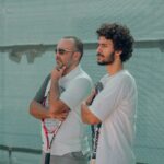 a couple of men stand near each other holding tennis rackets