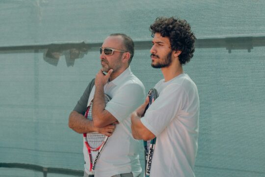 a couple of men stand near each other holding tennis rackets